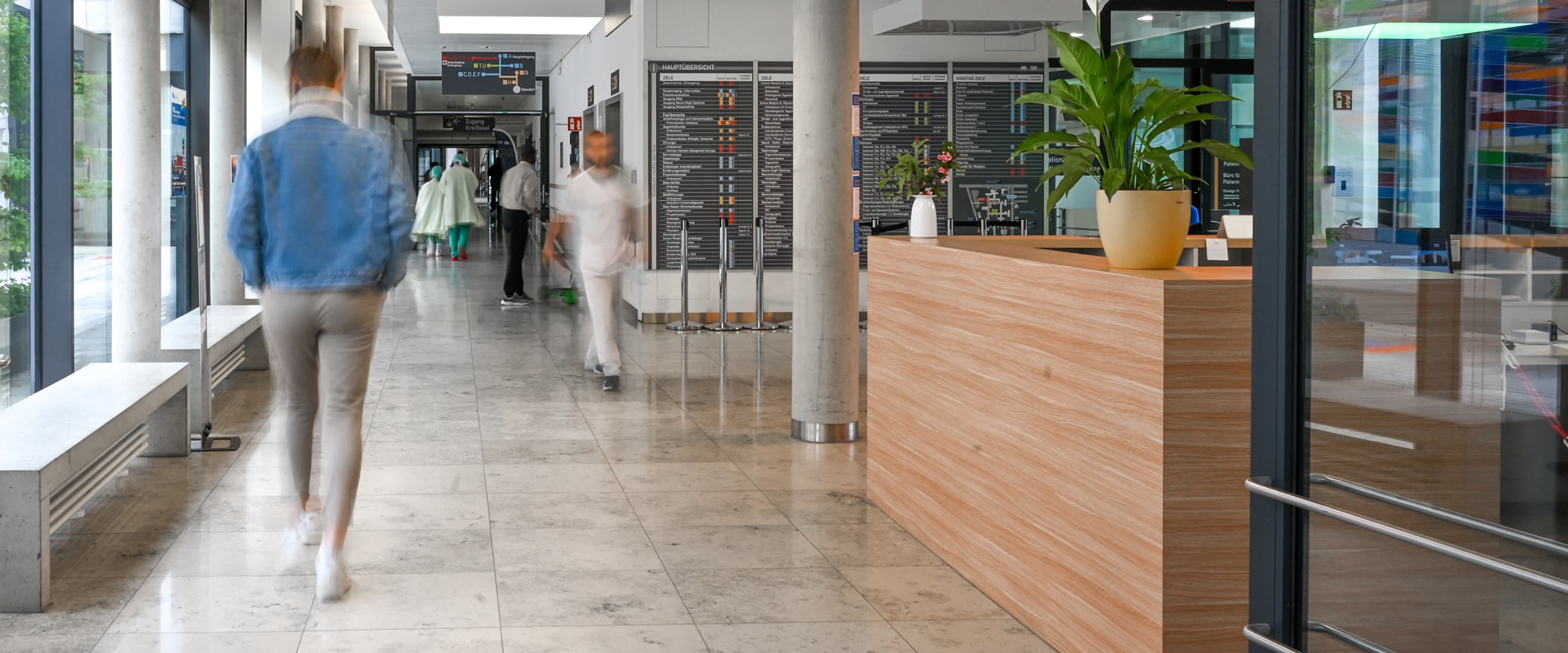 Mitarbeitende, Patientinnen und Patienten laufen durch einen Krankenhausflur