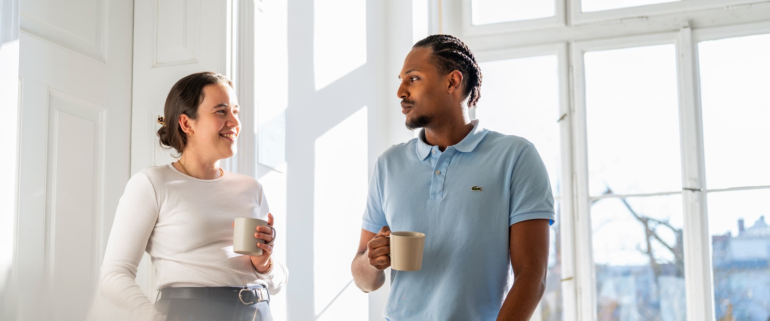 Ein Dualer Student spricht mit der Ansprechpartnerin für Duale Studenten, beide stehen mit einer Tasse Kaffee auf dem Flur