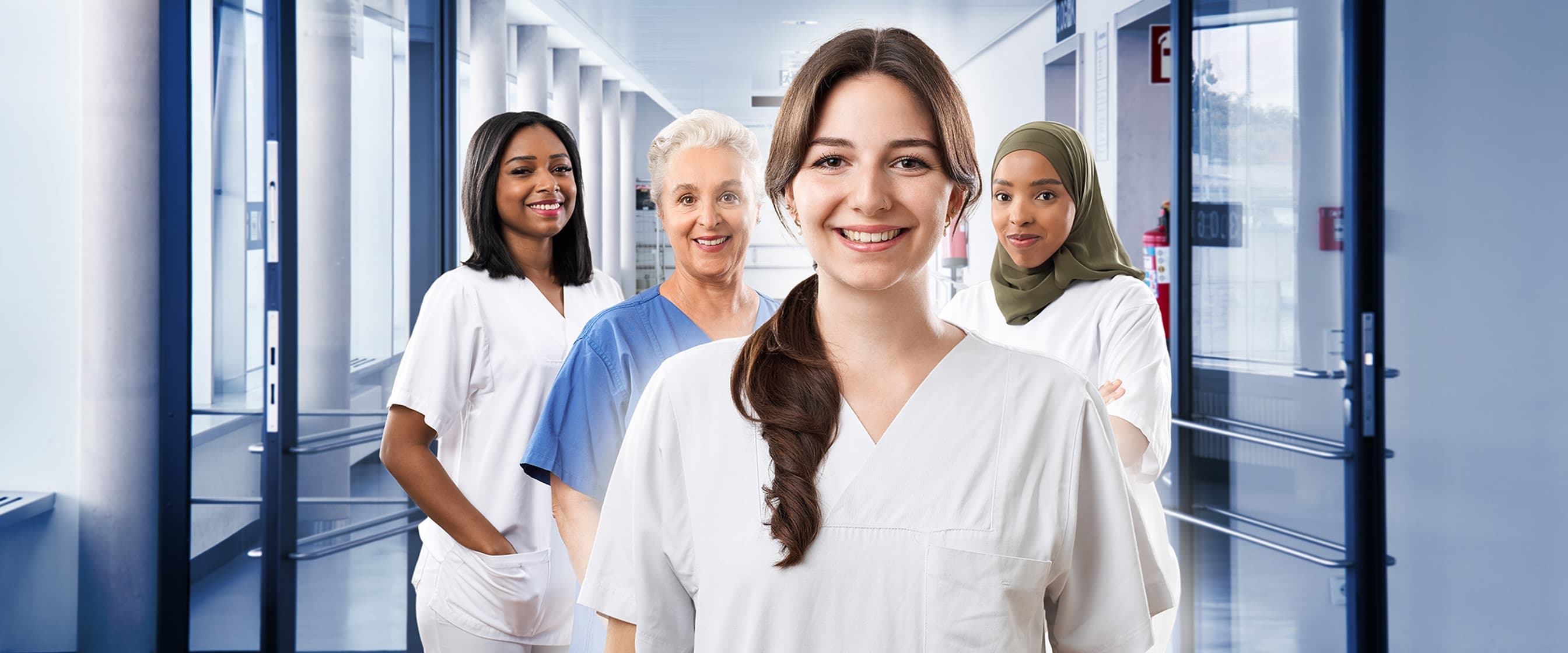 Vier Pflegefachkräfte stehen im Krankenhausflur und blicken in die Kamera