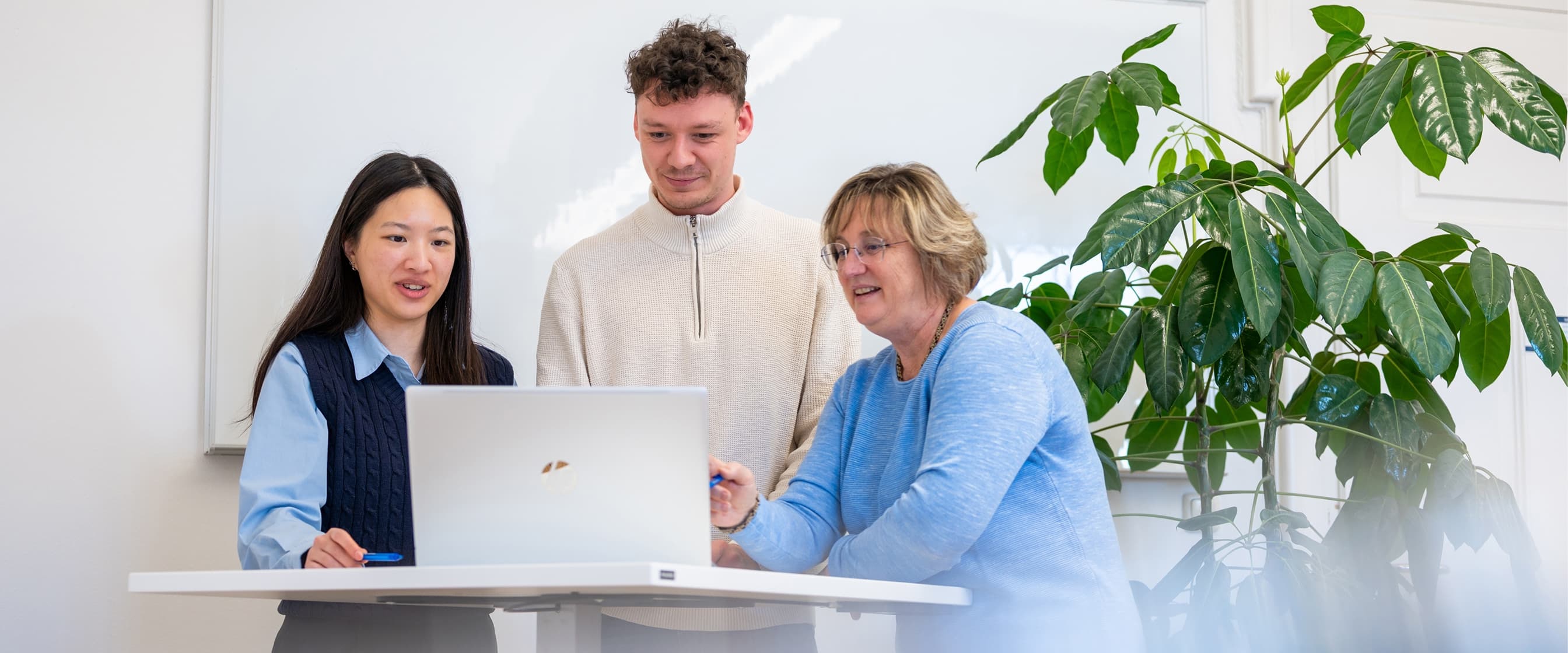 Drei Mitarbeitende aus der Verwaltung stehen an einem Stehtisch und besprechen ein Projekt am Laptop