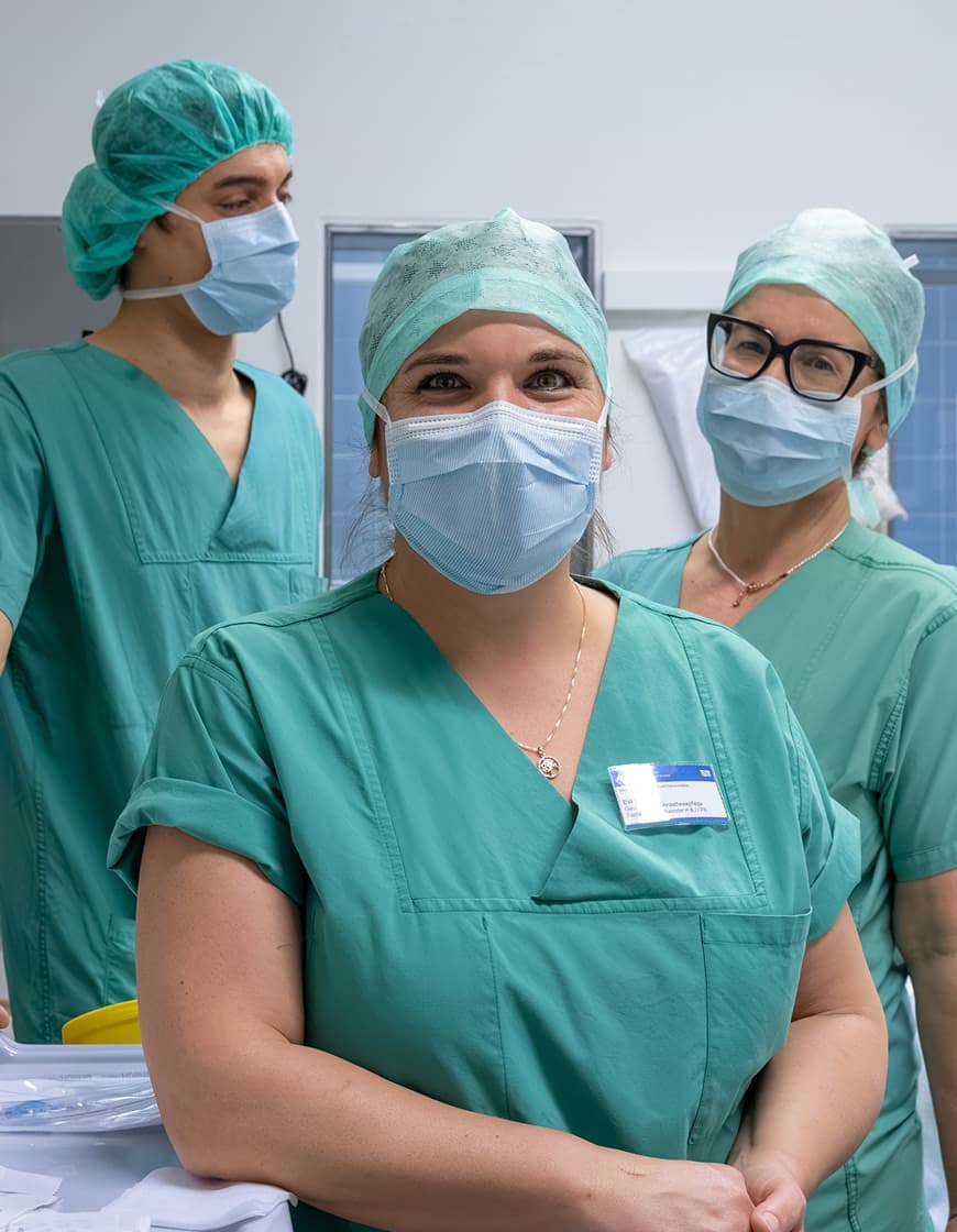 Drei ATAs stehen in der Gruppe zusammen, Evi, die Anästhesietechnische Assistentin im Vordergrund, blickt in die Kamera