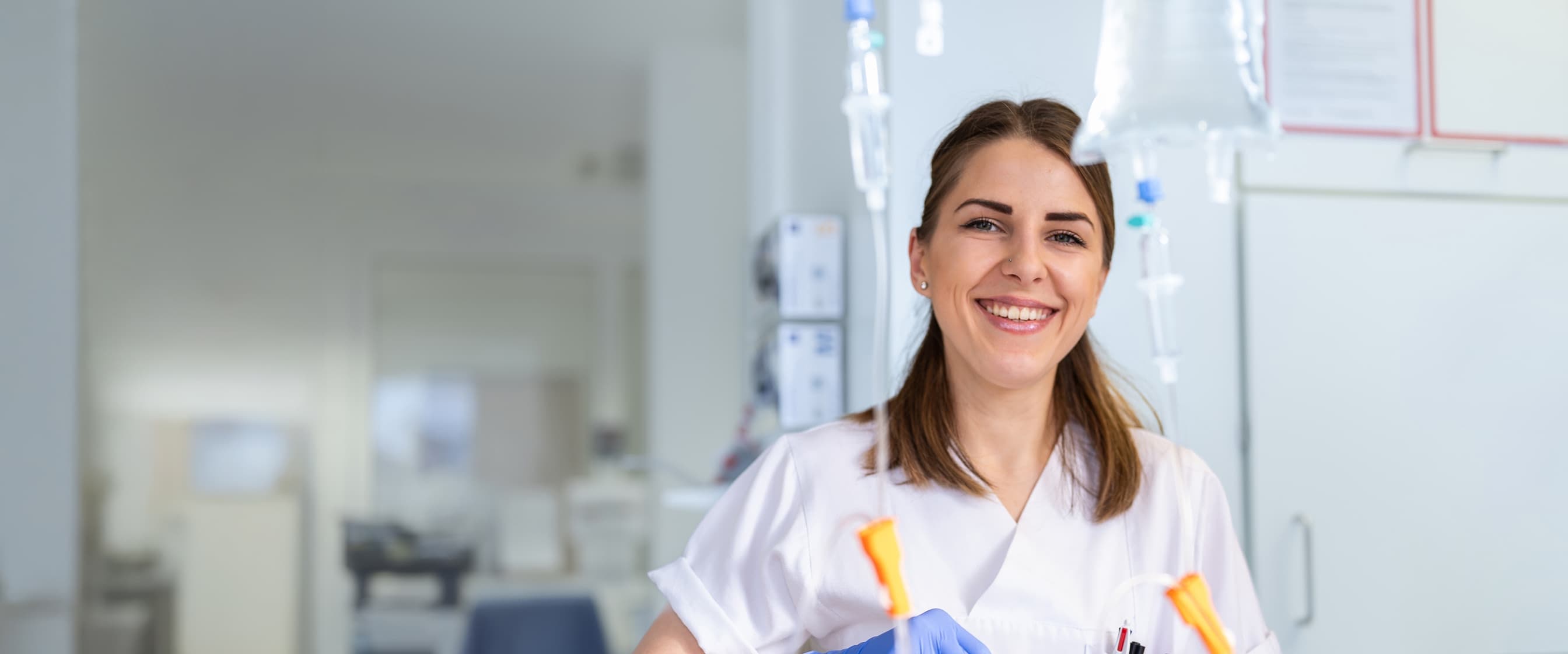 Eine Medizinische Fachangestellte hält eine Infusion in der Hand und blickt in die Kamera
